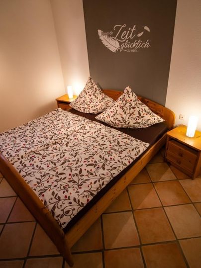 Ein gemütliches Schlafzimmer mit einem Holzbett und bunten Kissen. Neben dem Bett stehen Nachttische mit stilvollen Lampen.