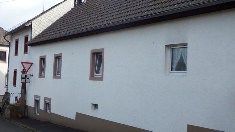 Ein einfaches Wohnhaus mit einem weißen Anstrich und einem braunen Sockel. Es gibt mehrere Fenster und ein Verkehrsschild in der Nähe.