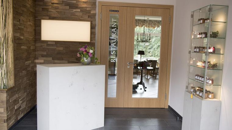 Ein modernes Restaurant mit einer eleganten Empfangstheke aus weißem Stein. Im Hintergrund sind Tischdecken und eine dekorative Vitrine mit Gläsern zu sehen.