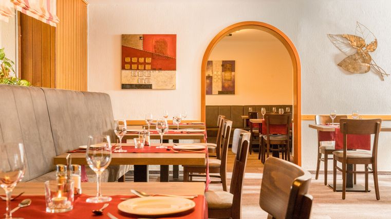 Ein gemütliches Restaurant mit Tischen und Stühlen in warmen Farben. Die Tische sind gedeckt und die Wände sind mit Kunstwerken dekoriert.
