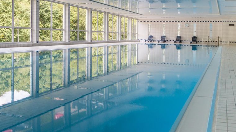 Ein helles Schwimmbad mit klarem Wasser und großen Fenstern. Die Umgebung ist modern und einladend.