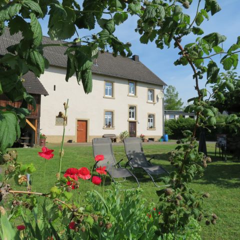 Ein schönes Haus mit einem gepflegten Garten. Zwei Liegen stehen im Grünen, umgeben von bunten Blumen.