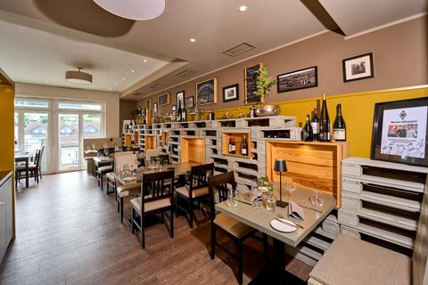 Ein modernes Restaurant mit Holzmöbeln und Weinfässern als dekorative Elemente. Die freundliche Atmosphäre wird durch große Fenster und sorgfältige Tischdekorationen unterstrichen.