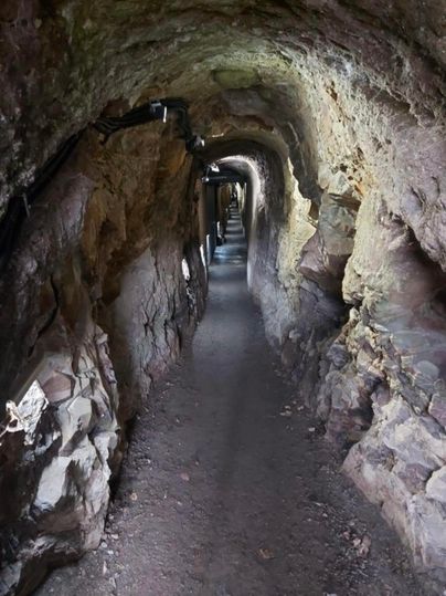 Ein schmaler Tunnel aus Fels, der von schwachem Licht erleuchtet wird. Der Weg ist gerade und etwa bis zur Hälfte sichtbar.