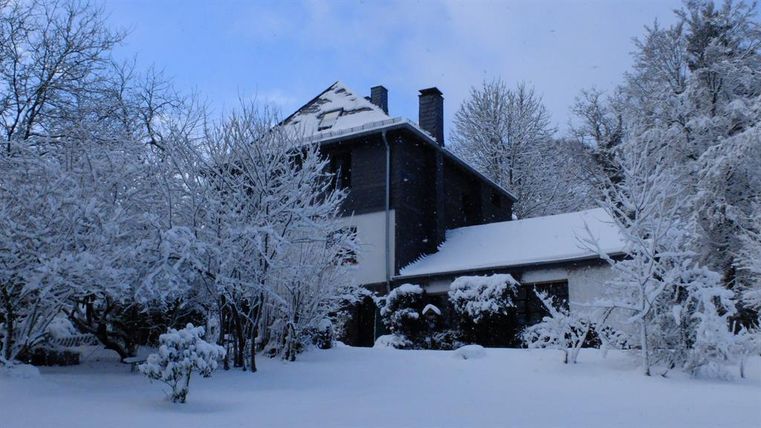 Ein Haus im Schnee, umgeben von schneebedeckten Bäumen. Der Himmel ist blau und klar.