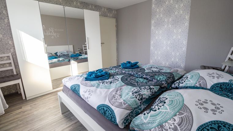 Ein modernes Schlafzimmer mit einem großen Bett und bunten Bettwäsche. Der Raum hat einen großen Spiegel und helle Wände, die ein einladendes Ambiente schaffen.