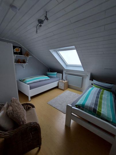 Ein gemütliches Schlafzimmer mit zwei Einzelbetten und einem Fenster im Dach. Die Wände sind hell, und es gibt einen kleinen Tisch und einen Stuhl.