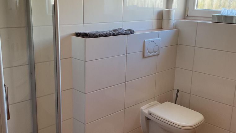 Ein modernes Badezimmer mit einer Dusche und einem WC. Die Wände sind gefliest und es gibt ein Fenster, das für natürliches Licht sorgt.
