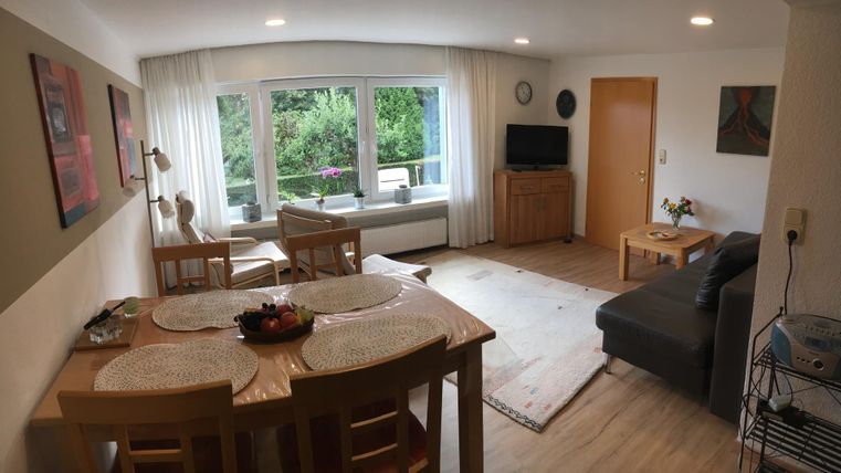 Ein gemütliches Wohnzimmer mit einem Essbereich und einem Sofa. Große Fenster bieten einen Blick auf die grüne Umgebung.