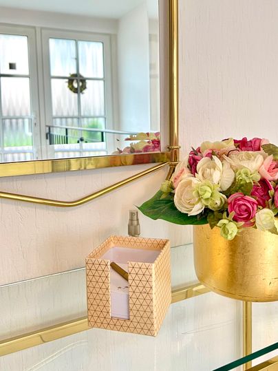 Ein schöner Raum mit einem goldenen Spiegel und einer Blumenvase. Auf dem Tisch steht eine dekorative Schachtel.