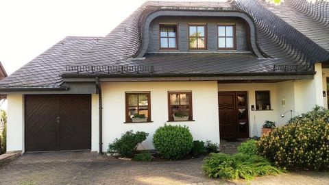 Ein modernes Haus mit einem schrägen Dach und großen Fenstern. Der Eingangsbereich ist von grünen Pflanzen umgeben.