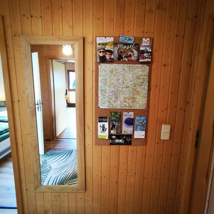 Ein Flurbereich mit holzgetäfelten Wänden, einer Spiegelwand und einem Informationsbrett. Das Brett zeigt Karten und Broschüren zu verschiedenen Aktivitäten.