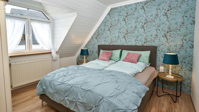 Ein gemütliches Schlafzimmer mit einem Doppelbett und bunten Kissen. Das Zimmer hat eine stilvolle Tapete und einen Blick aus einem Fenster.