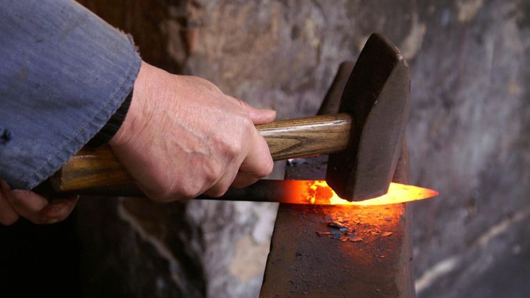 Ein Schmied bearbeitet ein glühendes Metallstück mit einem Hammer auf einem Amboss.