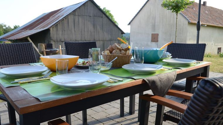 Ein schöner Tisch im Freien, gedeckt mit Geschirr und Gläsern. Im Hintergrund sind ländliche Gebäude zu sehen.