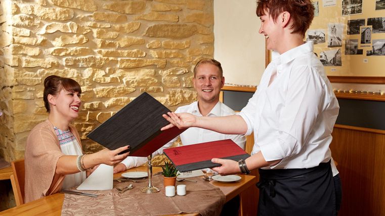 Ein Restaurantbesuch mit Gästen, die ein Menü erhalten. Ein Kellner serviert freundlich die Speisekarten an ein Paar am Tisch.