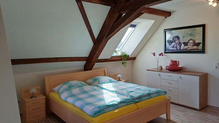 Ein Schlafzimmer mit einem großen Bett und bunten Bettdecken. Die Wände sind schräg, und es gibt einen Holzschrank sowie ein Bild an der Wand.