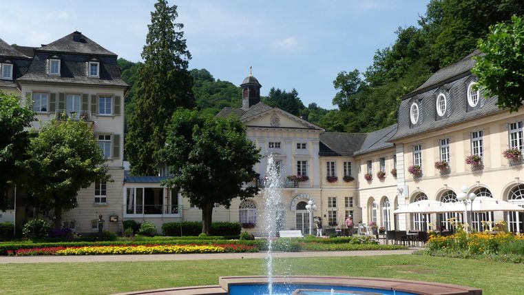 Ein schöner Innenhof mit einem Brunnen und gepflegten Gärten. Die umliegenden Gebäude sind im klassischen Stil gehalten.
