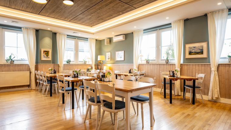 Ein stilvolles Restaurant mit Holzböden und hellen Wänden. Tische sind liebevoll gedeckt und große Fenster lassen viel Licht herein.