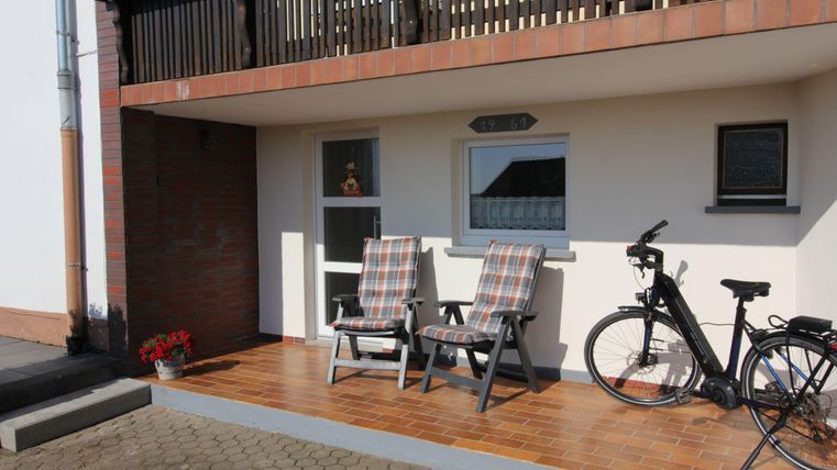 Ein Balkon mit zwei gemütlichen Liegestühlen und einem Fahrrad. Die Holzoberfläche und die blühenden Pflanzen verleihen dem Ort eine einladende Atmosphäre.