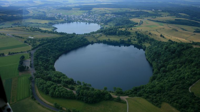Eine beeindruckende Luftaufnahme von zwei Seen, umgeben von üppigem Grün und sanften Hügeln. Die relaxte Landschaft vermittelt ein Gefühl von Ruhe und Naturnähe.