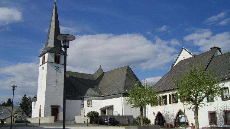A church with a tall tower stands next to a modern building. The sky is blue and there are no clouds visible.
