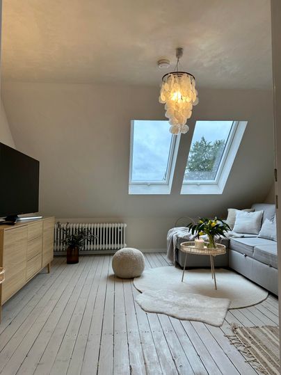 Ein modernes Wohnzimmer mit großen Dachfenstern und einem gemütlichen Sofa. Der Raum ist hell und einladend, mit einem eleganten Kronleuchter und sanften Farbtönen.