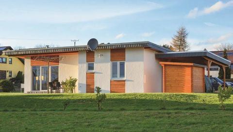 Ein modernes Haus mit einer Glasfront und Holzverkleidungen. Es befindet sich auf einer grünen Wiese in einer ruhigen Umgebung.