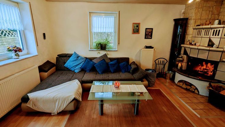 Ein gemütliches Wohnzimmer mit einem großen Sofa, bunten Kissen und einem modernen Tisch. Der Kamin verbreitet eine warme Atmosphäre.