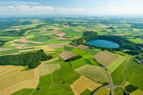 Eine weite Landschaft mit grünen Feldern und einem blauen See. Der Himmel ist klar und die Natur ist üppig.