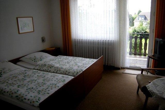 Ein einfaches Schlafzimmer mit zwei Einzelbetten und einem Balkon. Das Zimmer hat große Fenster mit Vorhängen und einen gemütlichen Schaukelstuhl.