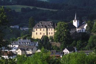 Ein malerisches Dorf mit historischen Gebäuden und einer Kirche. Im Hintergrund sind grüne Hügel und Bäume zu sehen.