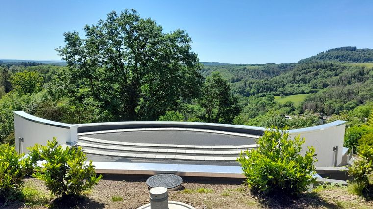 Ein moderner Aussichtspunkt mit einem halbkreisförmigen Geländer. Im Hintergrund erstreckt sich eine grüne Hügellandschaft unter klarem Himmel.