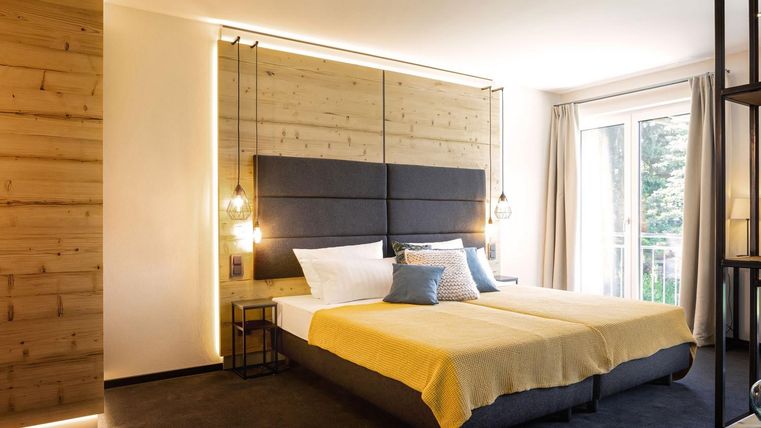 Ein modernes Schlafzimmer mit einem großen Bett und einer hellen, minimalistischen Einrichtung. Große Fenster bieten Tageslicht und einen Blick ins Freie.