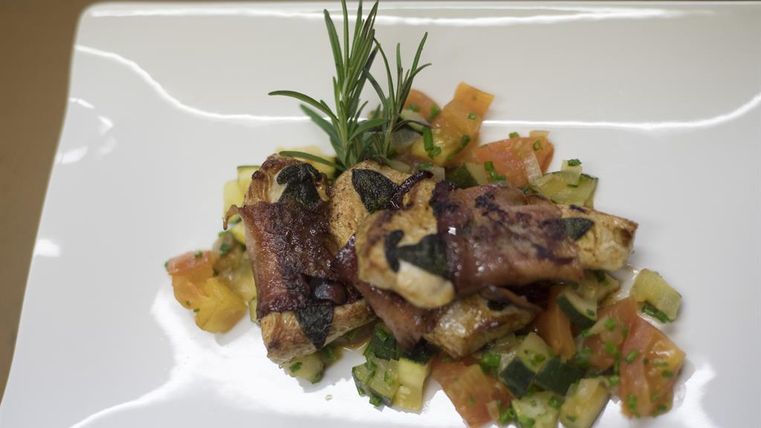 Ein gebratenes Gericht mit Kräutern auf einem Bett aus frischem Gemüse. Das Gericht ist schön angerichtet und wirkt appetitlich.