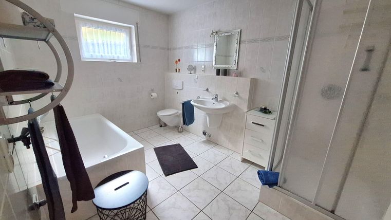 Ein modernes Badezimmer mit einer Badewanne, Dusche und Waschbecken. Die Wände sind hell gefliest, und es gibt einige Handtücher und Dekorationen.