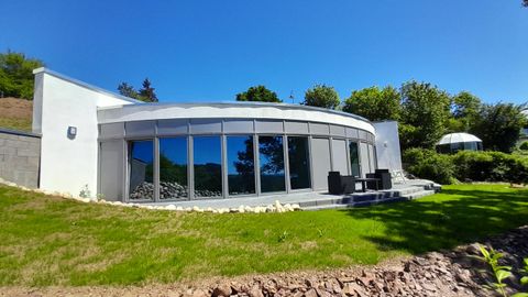 Ein modernes, rundes Haus mit großen Fenstern und einem schönen Garten. Die Umgebung ist grün und lichtdurchflutet.