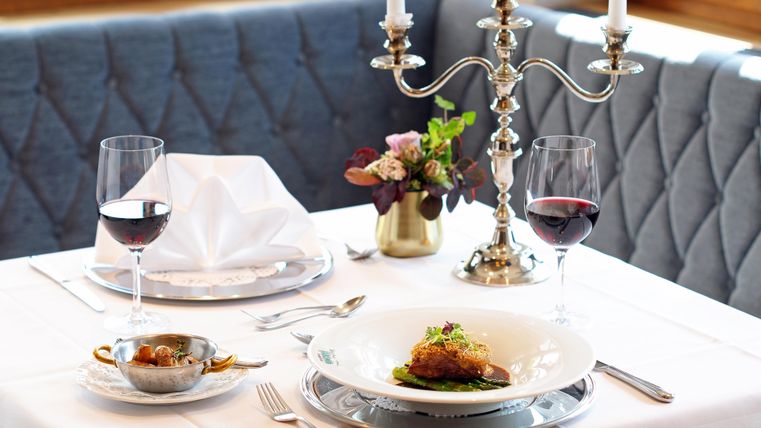 Ein elegant gedeckter Tisch mit einer schönen Speise in der Mitte. Zwei Weingläser und eine Blumendekoration runden das Bild ab.