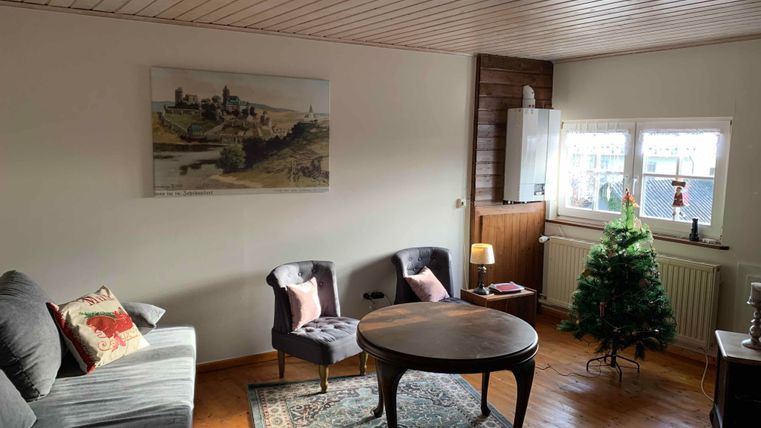 Ein gemütliches Wohnzimmer mit einem schönen Sofa und zwei Stühlen. Es gibt einen Tisch in der Mitte und einen kleinen Weihnachtsbaum in der Ecke.