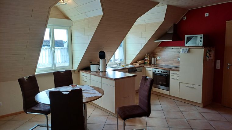 Eine moderne Dachgeschossküche mit schrägen Wänden. Der Essbereich besteht aus einem runden Tisch und Stühlen, umgeben von Fensterlicht.