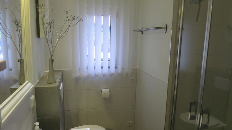 Ein modernes Badezimmer mit einer Dusche und einem großen Spiegel. Das Fenster mit Vorhängen lässt natürliches Licht herein.