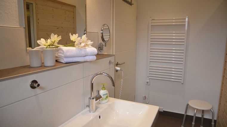 Ein modernes Badezimmer mit einem Waschbecken und einem großen Spiegel. Frische Handtücher und dekorative Blumen sorgen für eine einladende Atmosphäre.