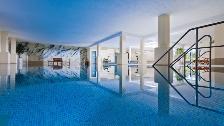 Ein eleganter Innenpool mit blauen Fliesen und klaren Wasser. Die Umgebung ist modern und einladend, mit natürlichen Lichtquellen.