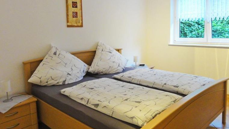 Ein einladendes Schlafzimmer mit einem großen Doppelbett und hellen Bettdecken. Das Zimmer hat ein Fenster, das Tageslicht hereinlässt.