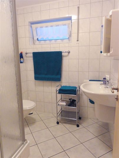 Ein modernes Badezimmer mit hellen Fliesen und einer Dusche. Blau-weiße Handtücher hängen am Handtuchhalter.