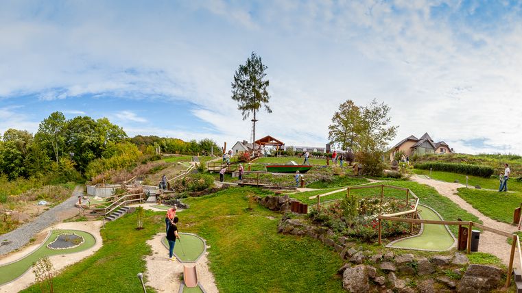 Panoramic picture of a miniature golf course with players and green landscape.