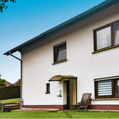 Ein modernes Haus mit einem gepflegten Garten. Die Fassade ist hell und einladend, umgeben von Bäumen und Rasenflächen.
