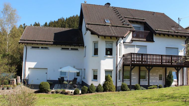 Ein modernes Haus mit einem großen Garten und Veranda. Die Sonne scheint und die Umgebung ist grün und einladend.