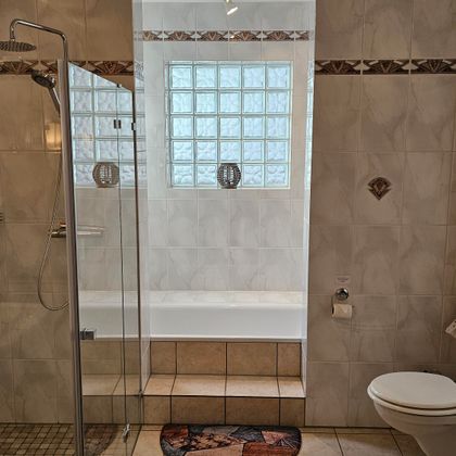 Ein modernes Badezimmer mit einer Dusche und einer Badewanne. Die Wände sind hell gefliest und es gibt natürliche Beleuchtung durch ein Fenster.