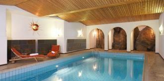 Ein eleganter Innenpool mit Holzdecke und warmem Licht. Entspannte Liegen laden zum Verweilen ein.